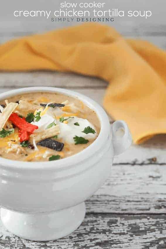 Creamy Chicken Tortilla Soup Slow Cooker Recipe topped with sour cream and tortilla strips in a white pedestal bowl with a yellow napkin behind it