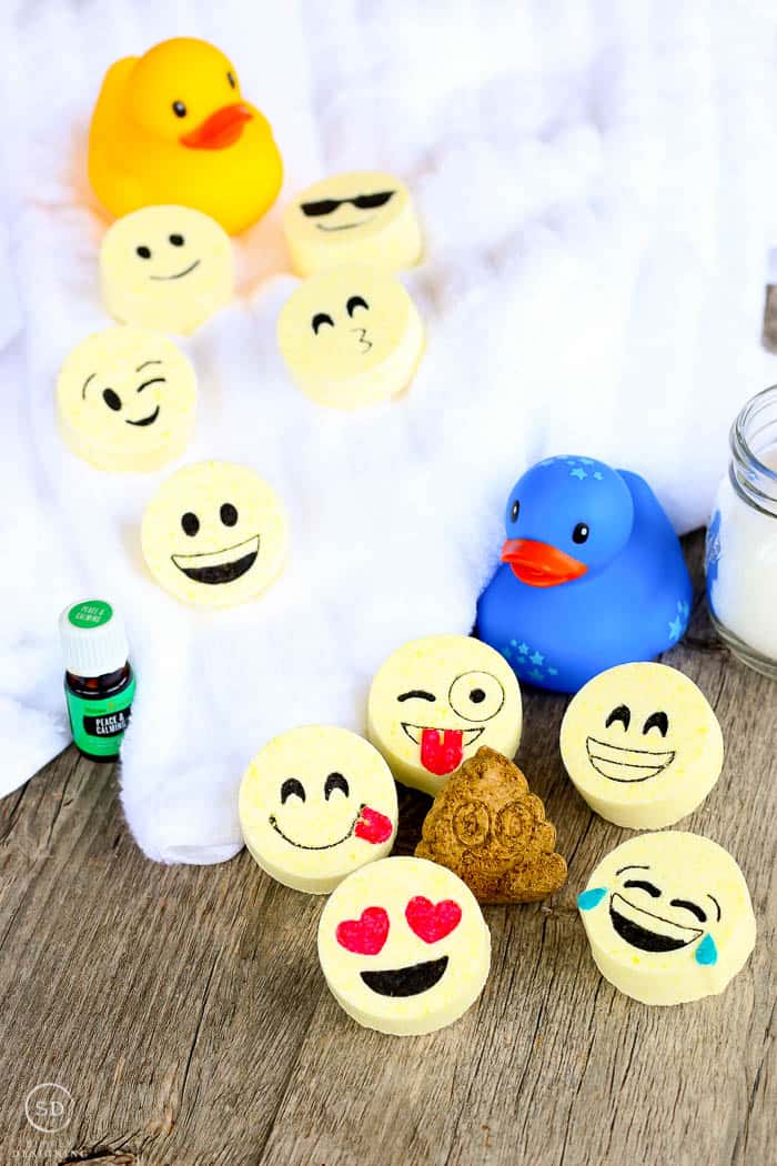 All the different kids bath bombs, this bath bomb recipe makes emoji faced tablets that you can drop in the bath. The finished bath bombs are surrounded by other bath essentials like towels and bath toys for kids. 