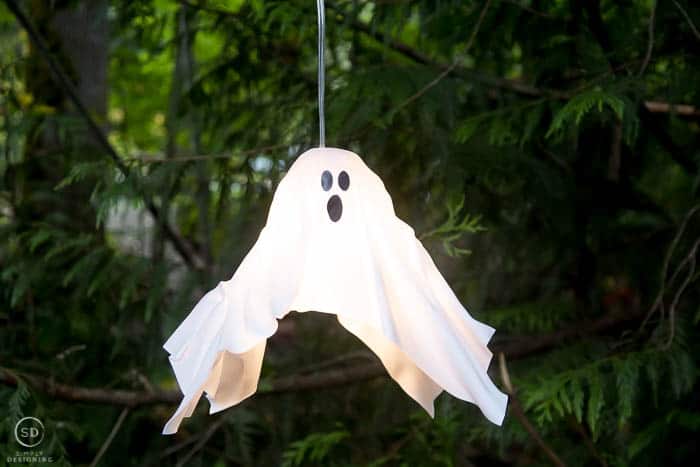 plastic white diy hanging ghost lantern hanging in a tree and turned on