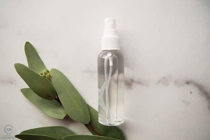 DIY Disinfecting Spray in a spray bottle with greenery on side