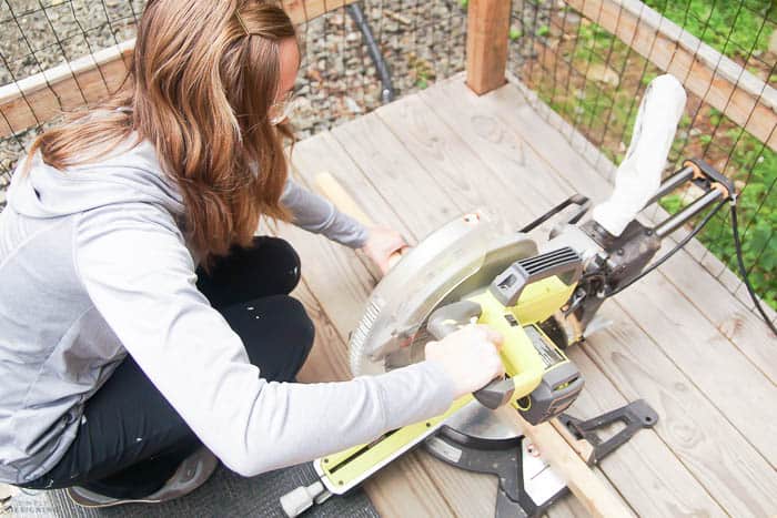 woman using a compound miter saw to cut boards