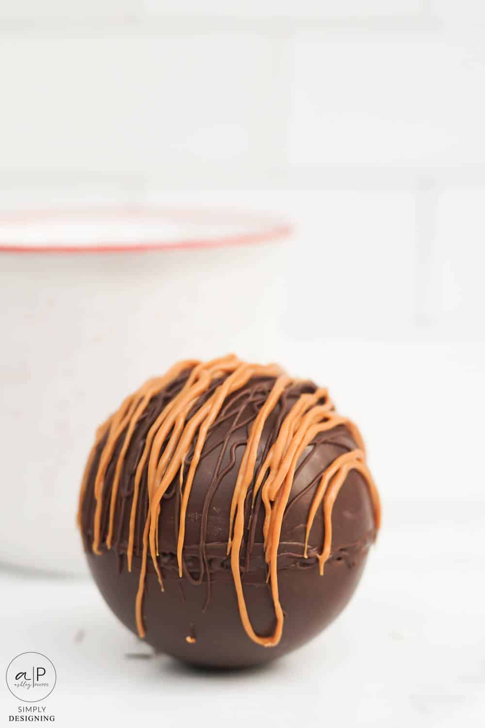 vertical photo of caramel hot chocolate bomb on a marble counter with a white mug in the background