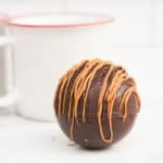 caramel hot cocoa bomb recipe with white mugs in the background